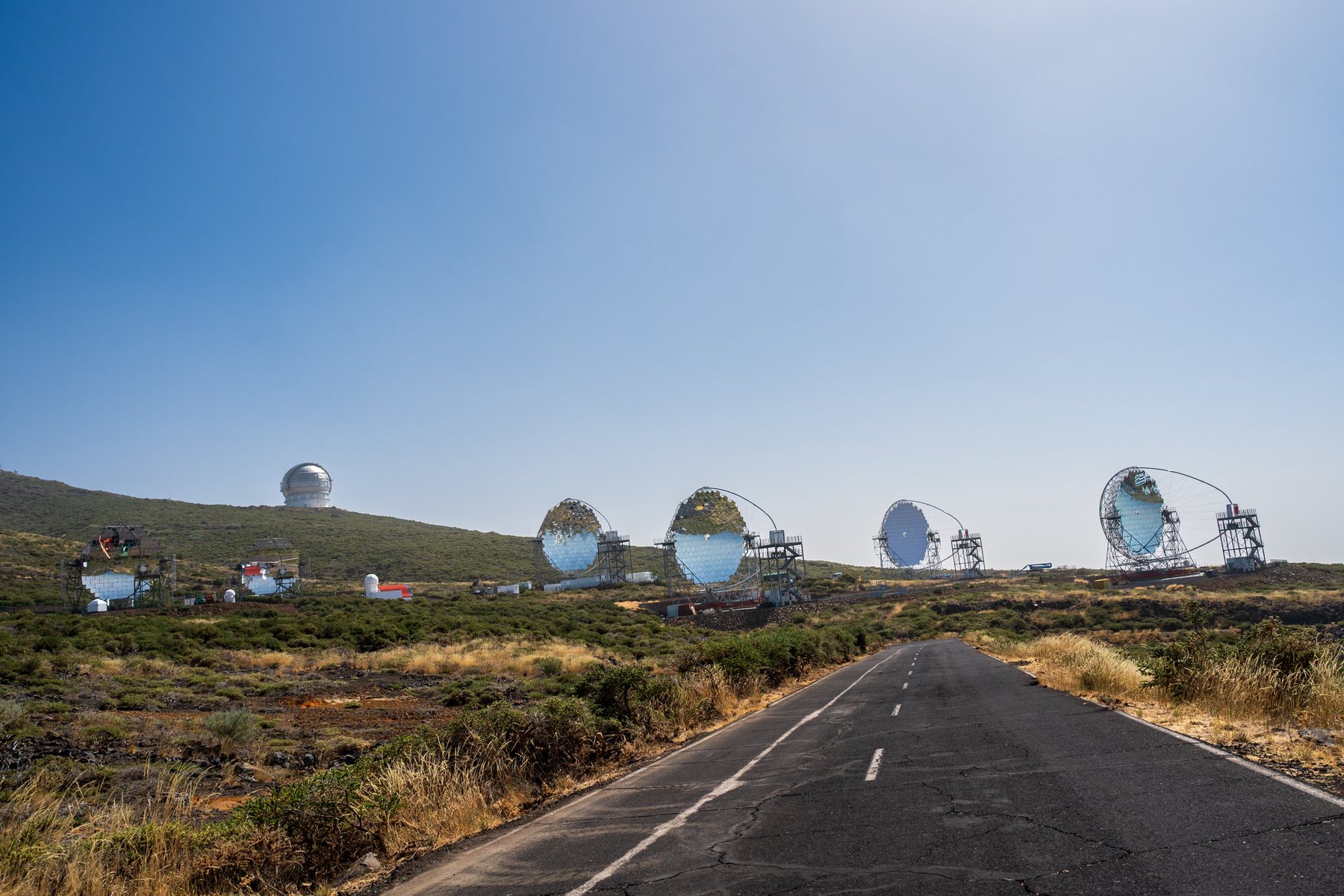 An empty mountain road approaching telescope domes and dishes at Roque de los Muchachos.