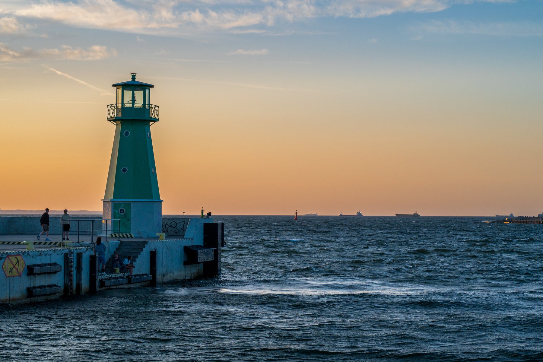 A green harbour light at the end of a pier with a red beacon across choppy water.