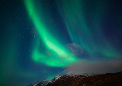 Vibrant green aurora borealis dancing across a starlit sky above a snow-capped mountain landscape in the Arctic night.