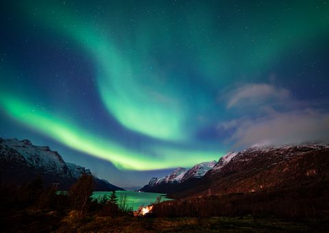 Vibrant aurora borealis dancing across the night sky above snow-capped mountains and a serene alpine lake, creating an ethereal green glow.