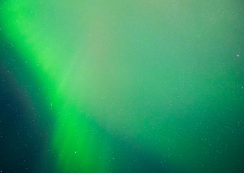 Vibrant aurora borealis with luminous green waves dancing across a starlit night sky, creating an ethereal natural light display.