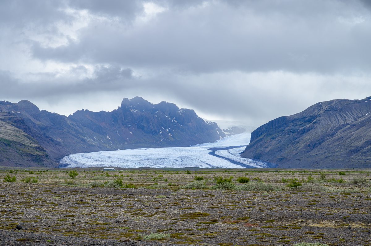 Blue-white ice curves through a rugged mountain valley, its dark moraine lines tracing the glacier’s slow movement.