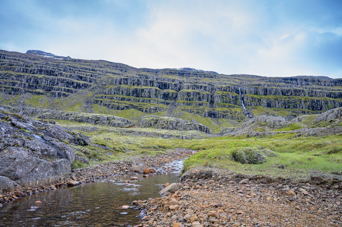 A shallow mountain stream winds toward a vast amphitheater of stacked volcanic ledges.