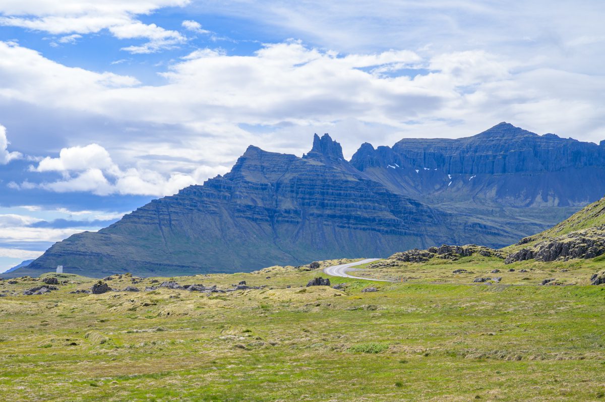 A winding road disappears toward a dramatic crown of jagged basalt spires.