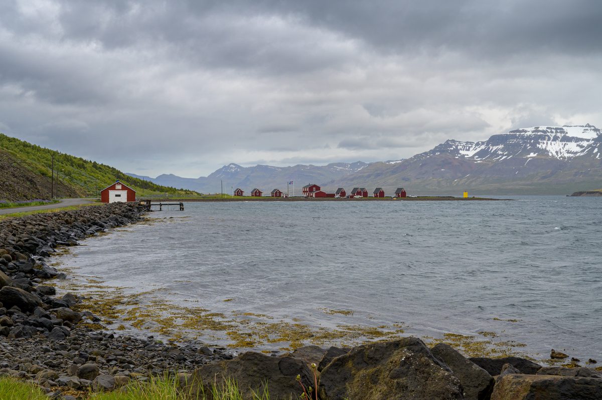 A line of red waterfront cabins gathers beneath snowy mountains as gray weather moves across the fjord.