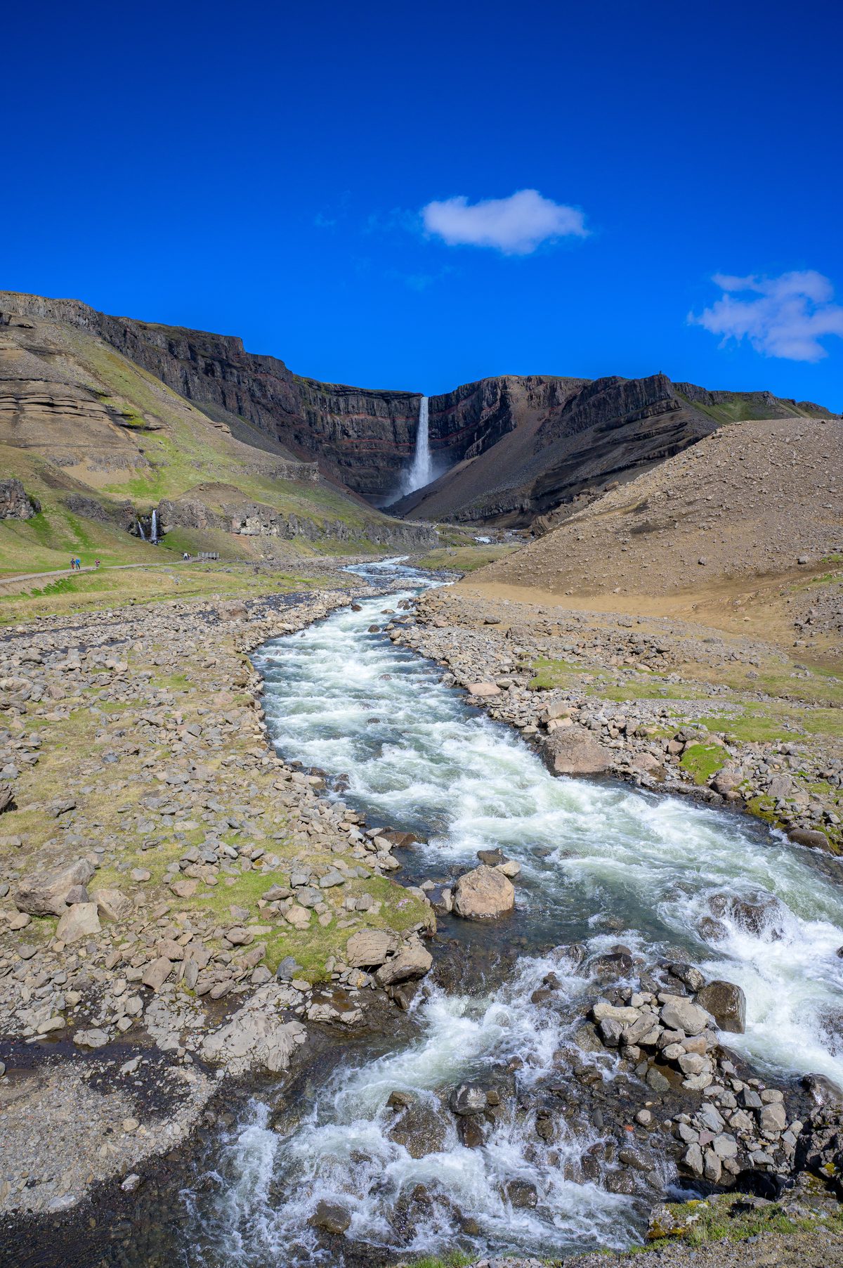 A vertical composition follows white water racing over dark rocks toward a distant waterfall.