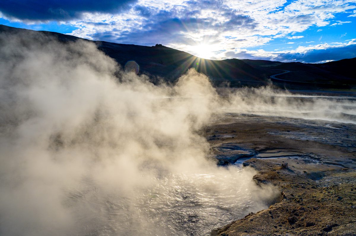 A dense plume of steam rises from the geothermal ground as the low sun breaks over a dark ridge.
