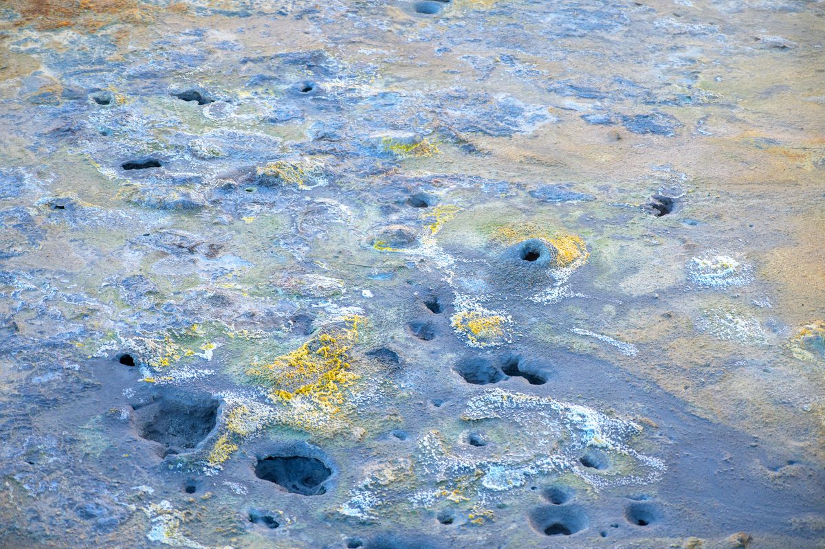 Small blue-gray mud vents and yellow mineral stains pattern the wet clay surface of Hverir.