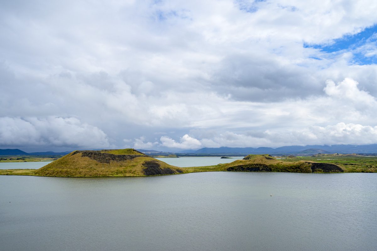 Rounded green pseudocrater islets sit in the calm gray-blue water of Mývatn below a dramatic rain-filled sky.