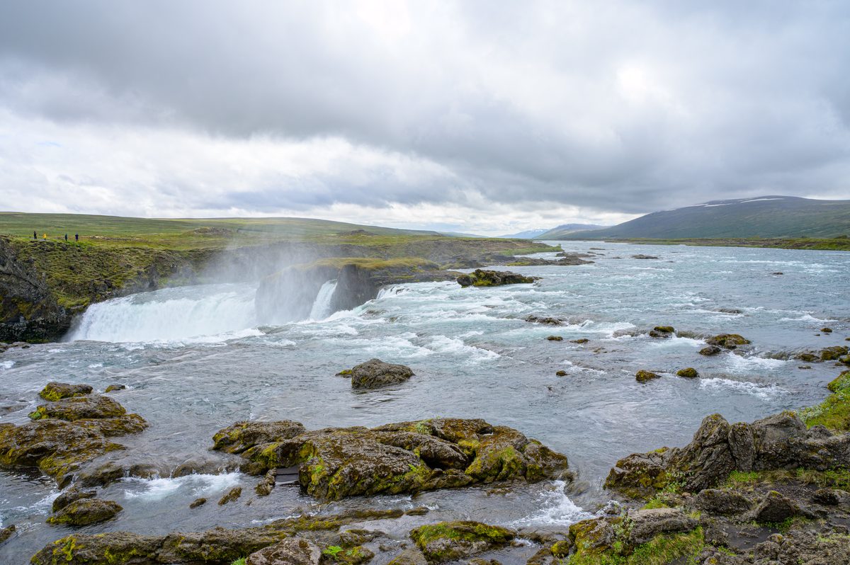 The Skjálfandafljót river spreads around mossy rocks before dropping over the broad ledges of Goðafoss.