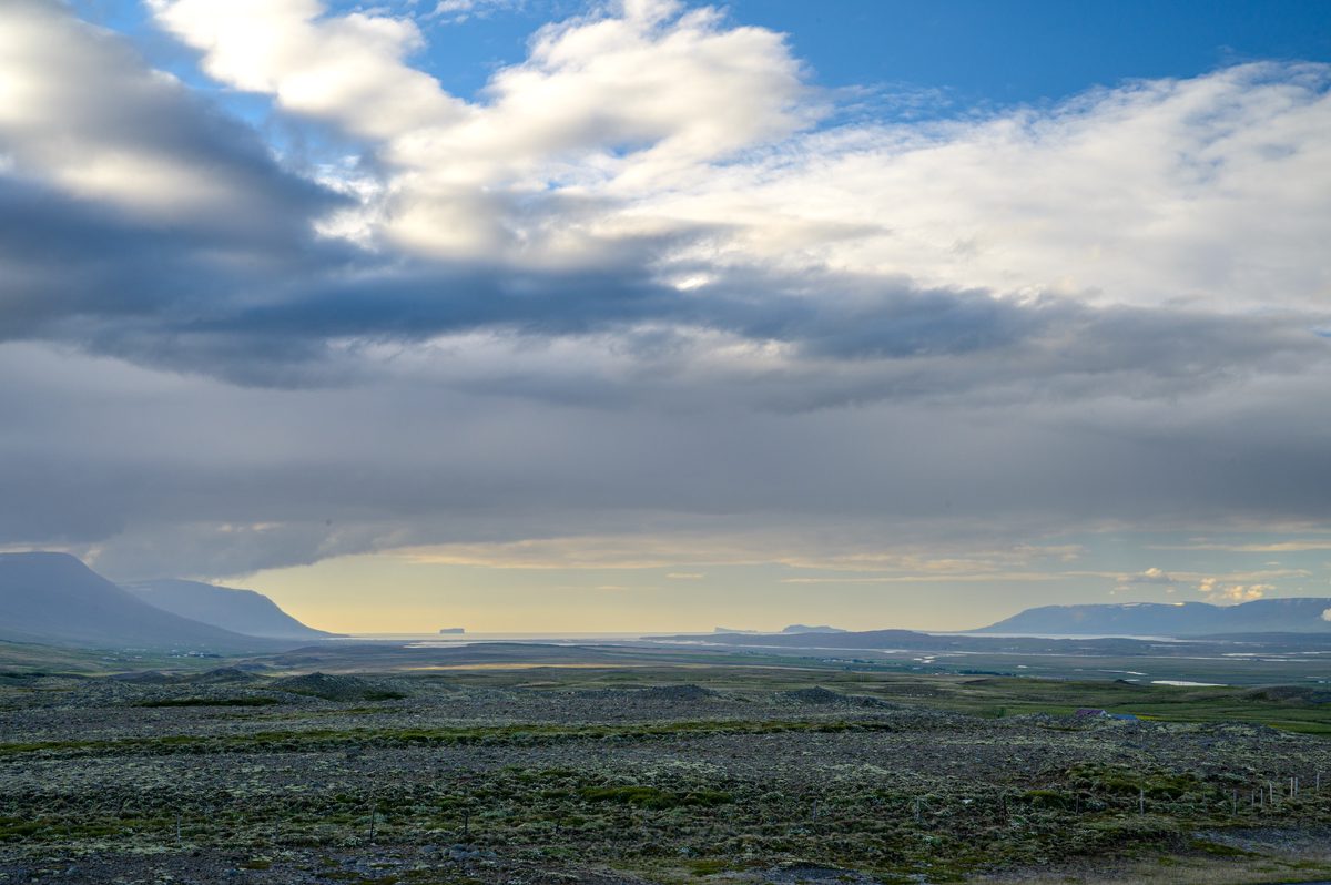 Sunlight breaks through layered clouds over a dark moss-covered plain and a distant chain of low mountains.